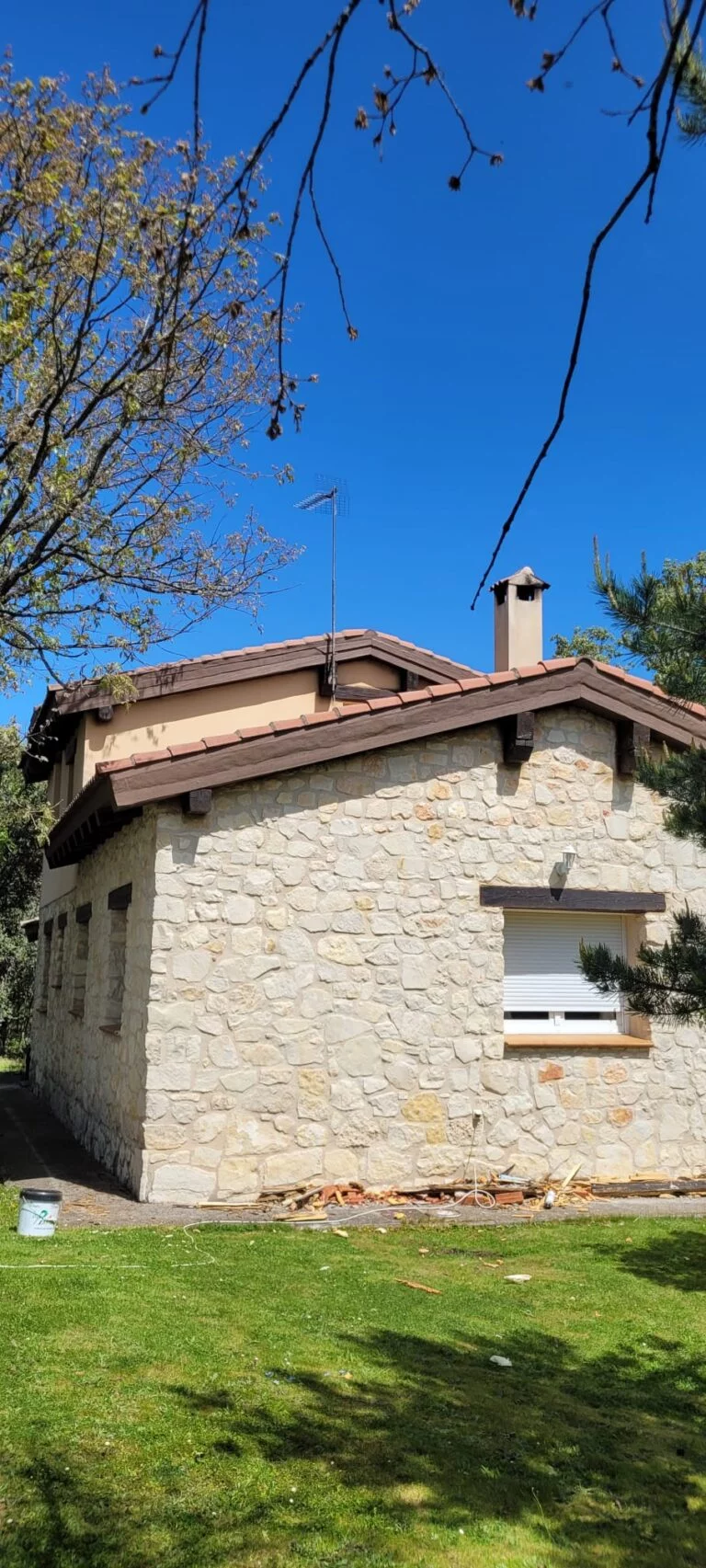 Casa de piedra con techo de tejas marrones y detalles de madera en la parte superior, con cielo azul de fondo.